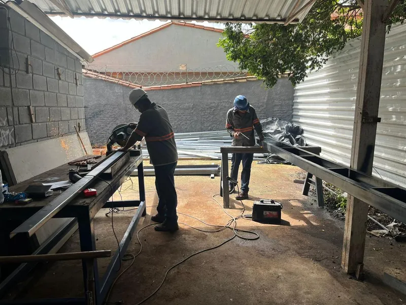 Montadores cortando e soldando perfis metálicos na bancada do canteiro