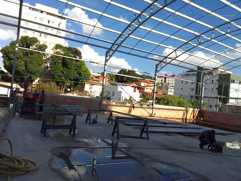 Arcos metálicos da cobertura do ginásio montados sobre a quadra, com cavaletes no piso