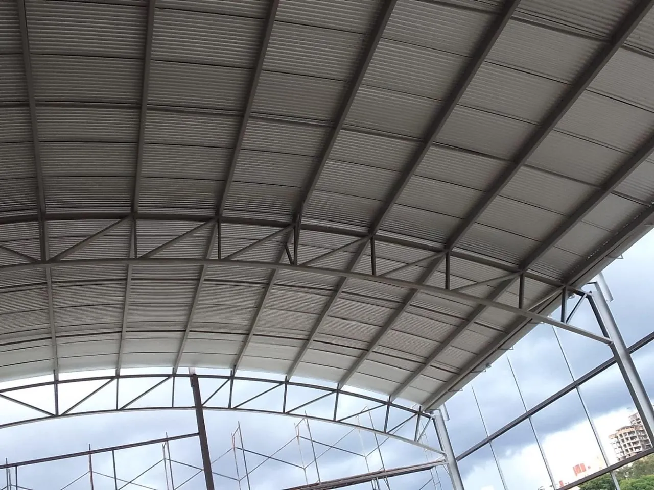 Cobertura do ginásio com telhas metálicas sobre os arcos treliçados