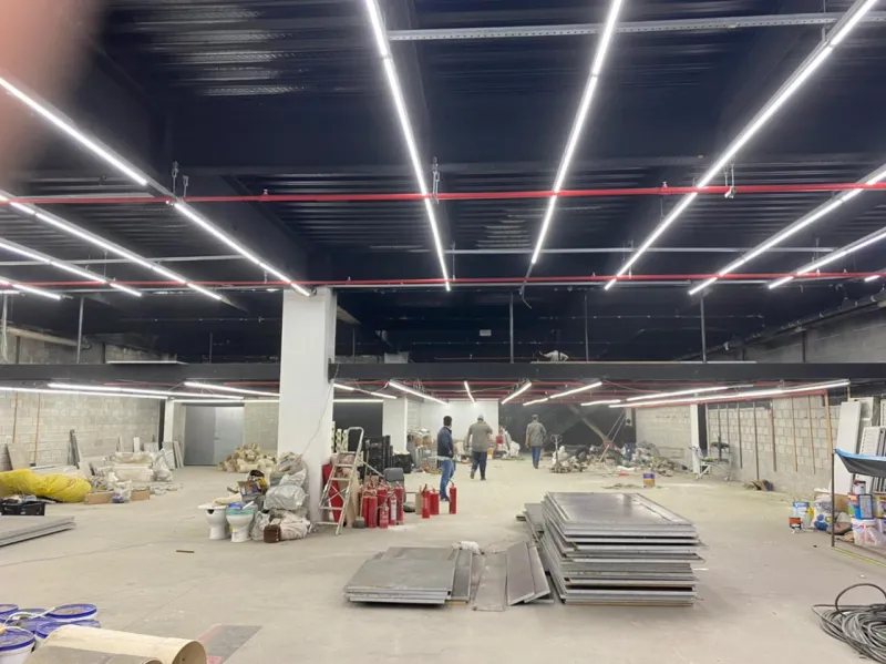 Salão da loja em obra, com o forro de luminárias lineares e materiais no piso