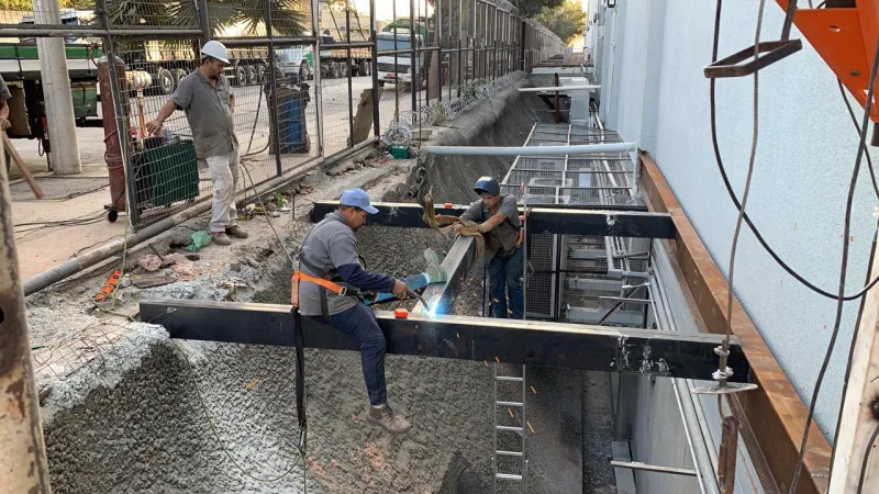 Montadores soldando a viga metálica sobre o vão
