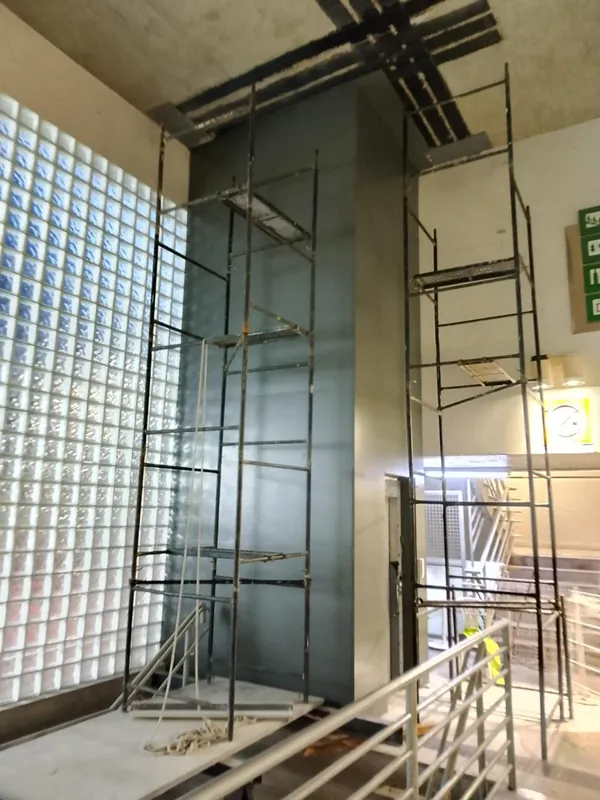 Torre do elevador revestida com painéis de ACM cinza, com andaimes ao redor