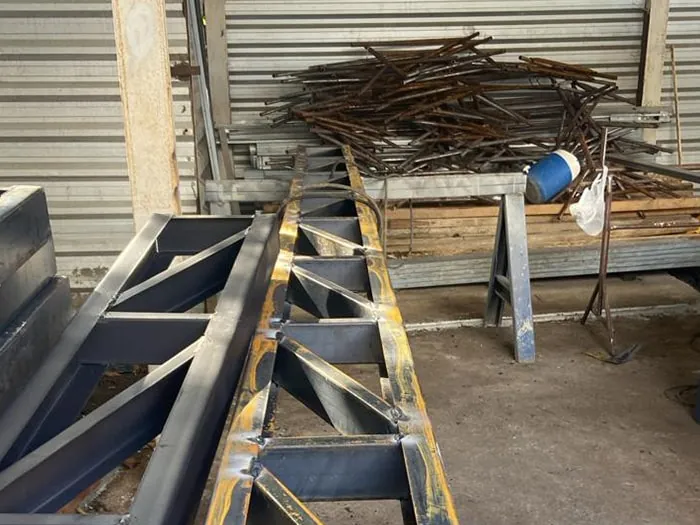 Treliça de reforço em fabricação sobre cavaletes, com sobras de vergalhões ao fundo