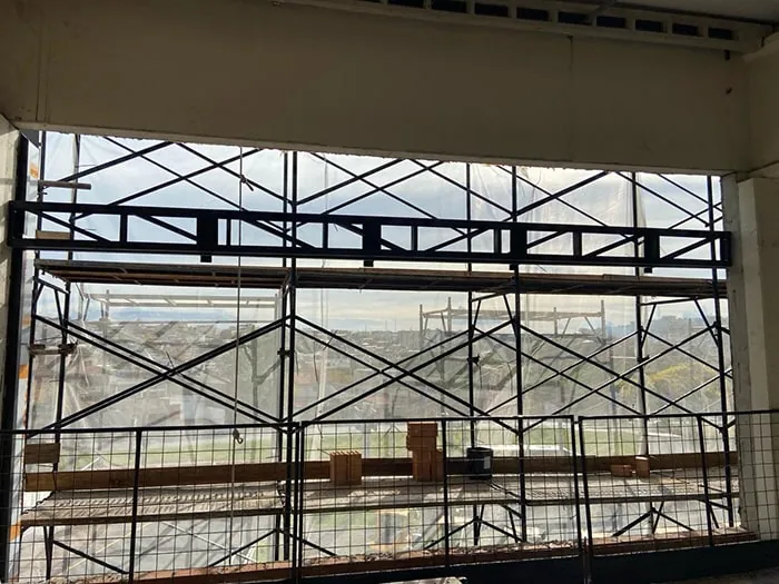 Treliça da cobertura e andaimes vistos de dentro do prédio, pela abertura da fachada