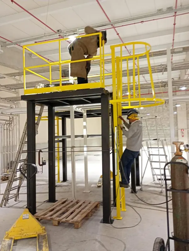 Equipe soldando o guarda-corpo amarelo de uma plataforma metálica